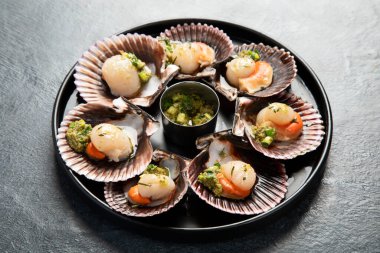 Koyu arkaplanda, siyah taş bir tabakta, soslu ve baharatlı deniz kabuklarıyla pişirilmiş deniz tarakları. Deniz ürünleri. Üst görünüm.