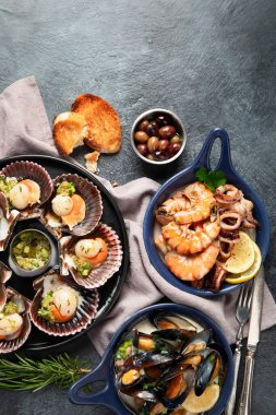 Koyu arkaplanda, siyah taş bir tabakta, soslu ve baharatlı deniz kabuklarıyla pişirilmiş deniz tarakları. Deniz ürünleri. Üst Manzara. Boşluğu kopyala.