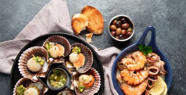 Koyu arkaplanda, siyah taş bir tabakta, soslu ve baharatlı deniz kabuklarıyla pişirilmiş deniz tarakları. Deniz ürünleri. Üst Manzara. Panorama.