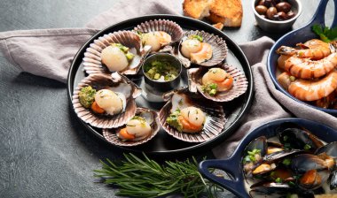 Koyu arkaplanda, siyah taş bir tabakta, soslu ve baharatlı deniz kabuklarıyla pişirilmiş deniz tarakları. Deniz ürünleri. Üst görünüm.