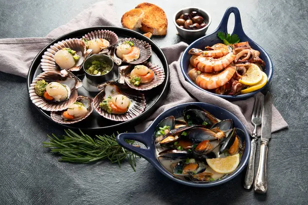 Koyu arkaplanda, siyah taş bir tabakta, soslu ve baharatlı deniz kabuklarıyla pişirilmiş deniz tarakları. Deniz ürünleri. Üst görünüm.