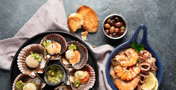 Koyu arkaplanda, siyah taş bir tabakta, soslu ve baharatlı deniz kabuklarıyla pişirilmiş deniz tarakları. Deniz ürünleri. Üst Manzara. Panorama.