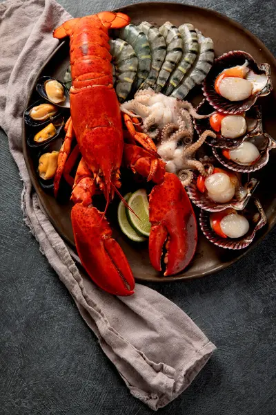 Taze ıstakoz, midye ve istiridye içeren deniz ürünleri tabağı. Karanlık bir arka planda okyanus gurmesi olarak. Üst görünüm.