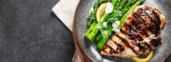 Izgara tavuk göğsü ve koyu arkaplanda kuşkonmaz. Üst Manzara. Kopyalama alanı olan Panorama.