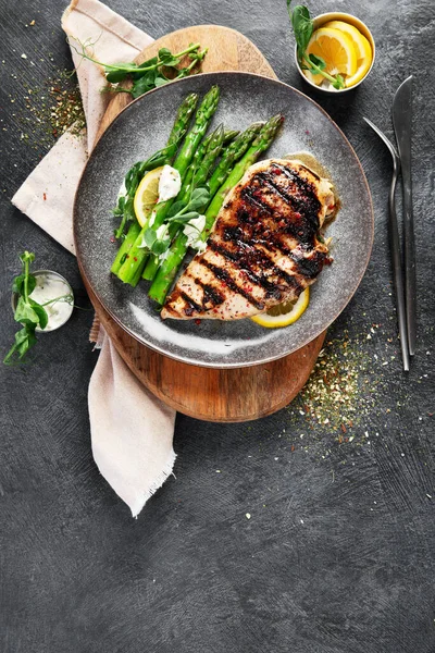 Izgara tavuk göğsü ve koyu arkaplanda kuşkonmaz. Üst görünüm.