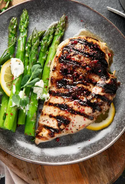 Izgara tavuk göğsü ve koyu arkaplanda kuşkonmaz. Üst görünüm.