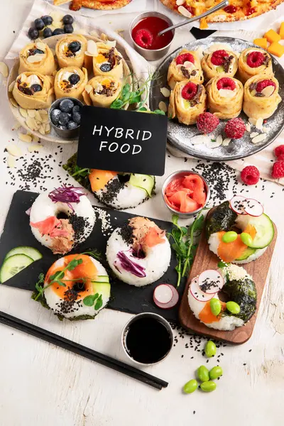 Hybrid trendy food on light wooden background, Sushi roll pancake, donut sushi, pizza with pasta. Top view