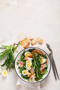 Karahindiba yapraklarından taze yaz salatası, yumurta, pastırma ve arka planda ekmek. Üst görünüm, alanı kopyala