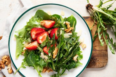Beyaz arka planda çilekli karahindiba salatası ve ceviz tabağı..