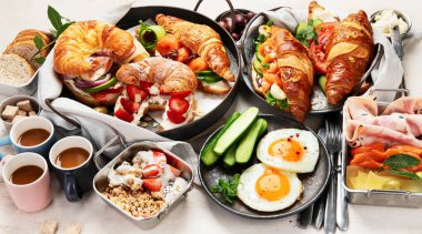 Kahvaltının yanında kahve, kruvasan, yumurta ve beyaz arka planda aperatifler var. Dengeli diyet. Üst görünüm.