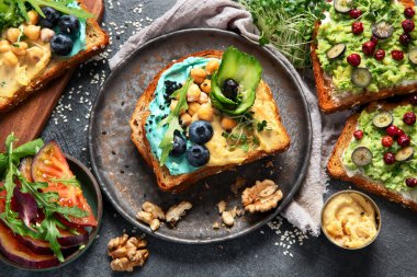 Humus, yabanmersini, avokado ve domatesli vejetaryen tostları. Karanlık arka planda nefis vejetaryen kahvaltısı. Üst görünüm