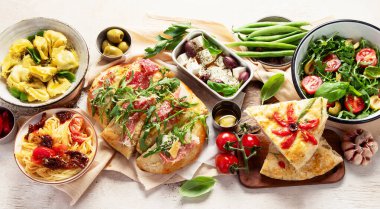 Tabaklar dolusu İtalyan yemeği pizza, makarna, ravioli, salata ve beyaz arka planda Focaccia. Üst görünüm