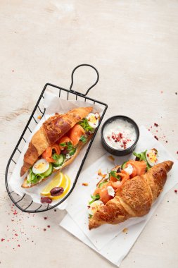 Hafif arka planda tuzlu ve sağlıklı kahvaltı. Krem peynirli taze somon kruvasanı, salatalık, yumurta ve salata. Üst görünüm, alanı kopyala