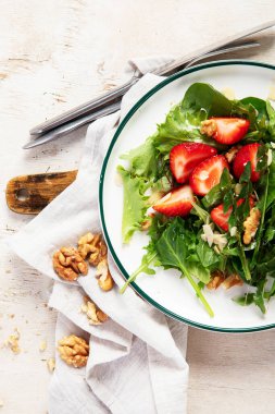 Beyaz arka planda çilekli karahindiba salatası ve ceviz tabağı..