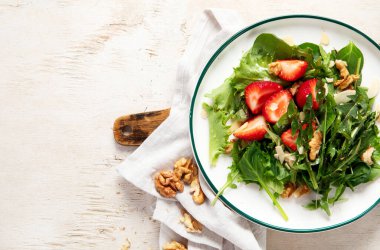 Beyaz arka planda çilekli karahindiba salatası ve ceviz tabağı..