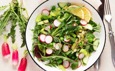 Karahindiba yapraklı taze salata, turp, ahşap arka planda salatalık. Üst görünüm, alanı kopyala