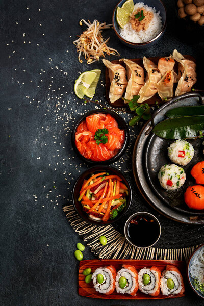 Суши и японская еда на тёмном фоне. Суши, суп, жареный рис, нигири, соевый соус, палочки для еды. Азиатско-японская пищевая рама. Вид сверху. Копирование пространства.
