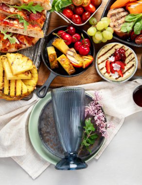 Yaz mangalı. Lezzetli ızgara yiyecekler. İki kişilik yemek. Biftek, pizza, böğürtlen, ışık masasında ananas. Üst görünüm