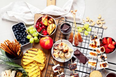 Izgara tatlı ve meyve çeşitleri. Yaz bbq masası. Ananas, şeftali, muz, marşmelov, çilek, hafif arkaplanda yabanmersini. Üst görünüm