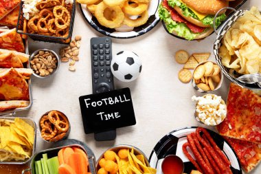 Futbol atıştırmalıkları masası. Maç zamanı. Pizza, burger, patlamış mısır, fındık ve top ahşap arka planda. Üst görünüm, alanı kopyala