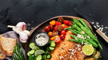 Taze sebzeli, limonlu ve az pişmiş somon balığı. Koyu arkaplanda pişmiş balık. Üst görünüm, alanı kopyala