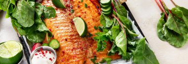 Taze yeşillik ve limonla pişirilmiş somon balığı. Hafif ahşap arka planda pişmiş kırmızı balık. Pankart