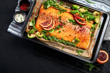 Siyah arka planda pişmiş deniz ürünleri. Fırında somon, soğan, limon, nar suyu. Üst görünüm