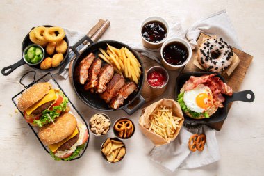 Çeşitli Amerikan yemekleri, patates kızartmaları, hamburgerler, cipsler, patlamış mısır, abur cuburlar ve soslar beyaz arka planda..