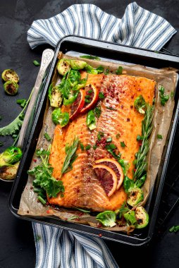 Siyah arka planda pişmiş deniz ürünleri. Fırında somon, soğan, limon, nar suyu. Üst görünüm