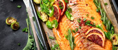 Siyah arka planda pişmiş deniz ürünleri. Fırında somon, soğan, limon, nar suyu. Üst görünüm