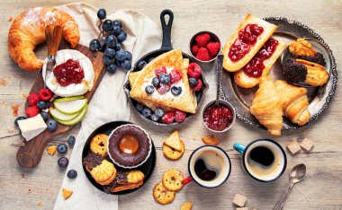 Üzerinde çeşitli Fransız kurabiyeleri, krepler, böğürtlenler, ahşap arka planda kruvasanlar olan bir masa. Lezzetli tatlı masası. Üst görünüm.