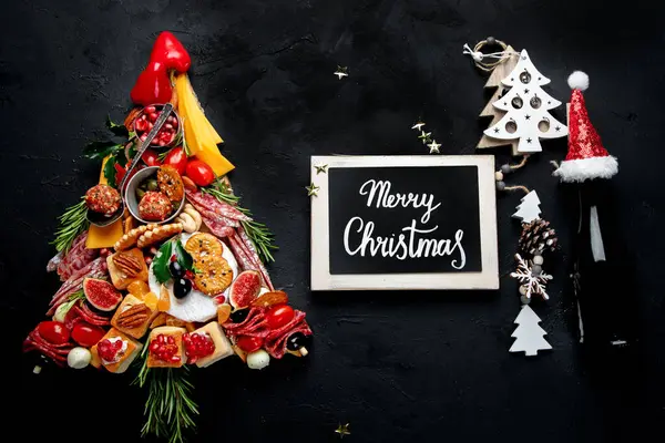 İçinde kraker, peynir, domates ve kızılcık olan Noel ağacı, arka planda kış tatili atıştırmaları. Tatil yemeği. Üst görünüm.