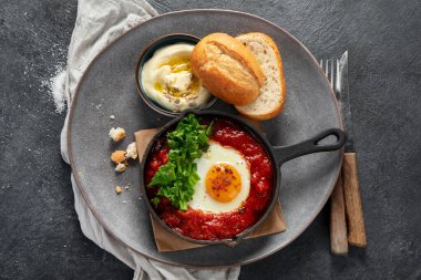 Shakshuka yumurtaları ve siyah bir arka planda ekmek. Baharatlı domates soslu haşlanmış yumurta. Geleneksel Yahudi omleti. Üst görünüm.