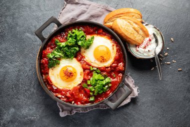 Shakshuka yumurtaları ve siyah bir arka planda ekmek. Baharatlı domates soslu haşlanmış yumurta. Geleneksel Yahudi omleti. Üst görünüm.