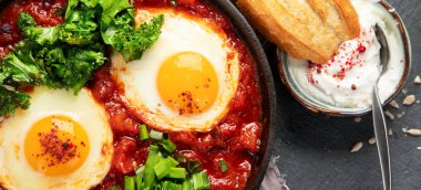 Shakshuka yumurtaları ve siyah bir arka planda ekmek. Baharatlı domates soslu haşlanmış yumurta. Geleneksel Yahudi omleti. Üst Manzara. Panorama.