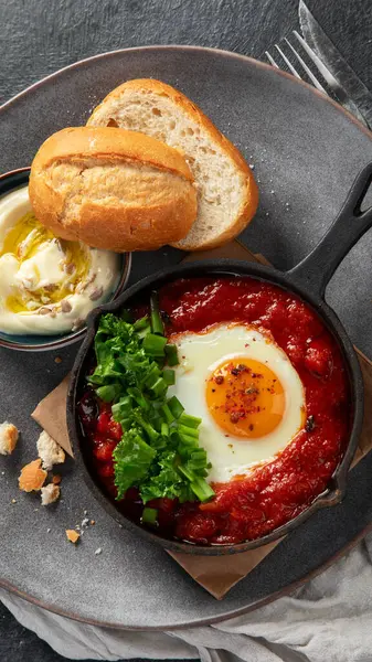 Shakshuka yumurtaları ve siyah bir arka planda ekmek. Baharatlı domates soslu haşlanmış yumurta. Geleneksel Yahudi omleti. Üst görünüm.