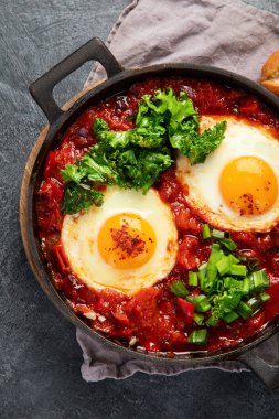 Shakshuka yumurtaları ve siyah bir arka planda ekmek. Baharatlı domates soslu haşlanmış yumurta. Geleneksel Yahudi omleti. Üst görünüm.