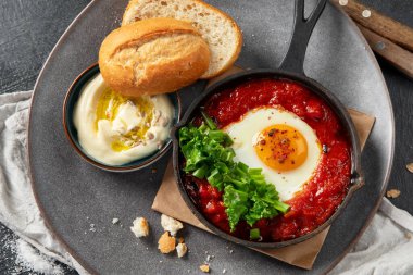 Shakshuka yumurtaları ve siyah bir arka planda ekmek. Baharatlı domates soslu haşlanmış yumurta. Geleneksel Yahudi omleti. Üst görünüm.