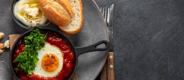 Shakshuka yumurtaları ve siyah bir arka planda ekmek. Baharatlı domates soslu haşlanmış yumurta. Geleneksel Yahudi omleti. Üst Manzara. Kopyalama alanı olan Panorama.