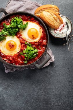 Shakshuka yumurtaları ve siyah bir arka planda ekmek. Baharatlı domates soslu haşlanmış yumurta. Geleneksel Yahudi omleti. Üst Manzara. Boşluğu kopyala.