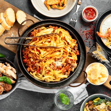 Bolonez soslu makarna, mantı, tavuk soslu makarna, parmesan peyniri ve koyu arkaplanda su. Üst görünüm.