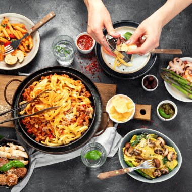 Bolonez soslu makarna, mantı, tavuk soslu makarna, parmesan peyniri ve koyu arkaplanda su. Üst görünüm.