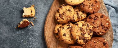 Koyu arka planda, ahşap tabakta çeşitli çikolatalı kurabiyeler..