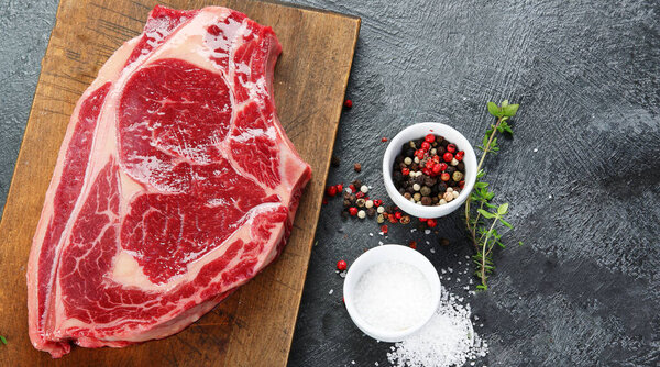 Raw  meat Ribeye Steak with pepper and salt on dark background, top view.