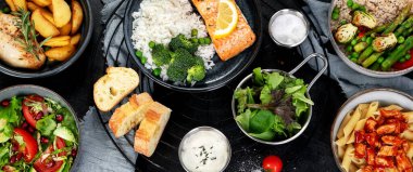 Bir dizi ana yemek. Farklı sağlıklı ana yemekler, et ve balık yemekleri, makarna, salatalar, soslar, arka planda ekmek ve sebzeler. Üst Manzara. Panorama.