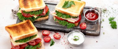 Peynirli sandviç, jambon, domates ve taze salata. Tahta bir tahtanın üzerinde çıtır çıtır ekmek ve soslu beyaz arka plan, üst manzara. Panorama.