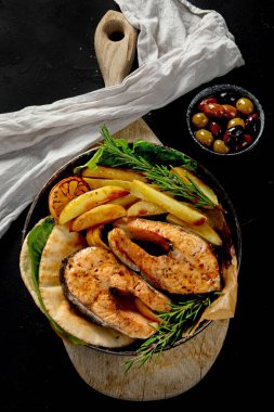 Pişmiş somon bifteği ve kızarmış patatesler siyah arka planda servis ediliyor. Sağlıklı beslenme. Üst görünüm.