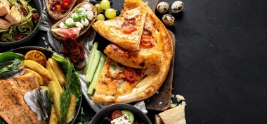 Çeşitli Akdeniz yemekleri - balık, deniz ürünleri, soslar, makarna, atıştırmalıklar, siyah arka planda pizza. Üst Manzara. Kopyalama alanı olan Panorama.