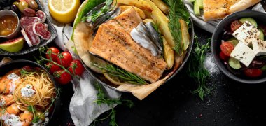 Çeşitli Akdeniz yemekleri - balık, deniz ürünleri, soslar, makarna, atıştırmalıklar, siyah arka planda pizza. Üst görünüm. 