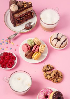 Üzerinde çeşitli kurabiyeler, çörekler, kekler, peynirli kekler ve pembe arka planda kahve fincanları olan masa. Lezzetli tatlı masası.. 